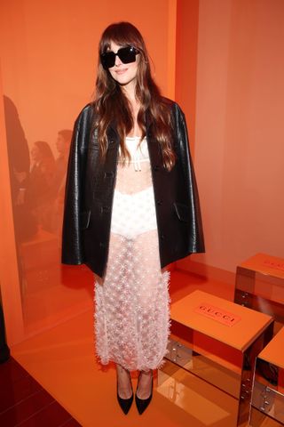 Dakota Johnson wearing a sheer white dress and black leather jacket at the Gucci Spring 2025 show in Milan